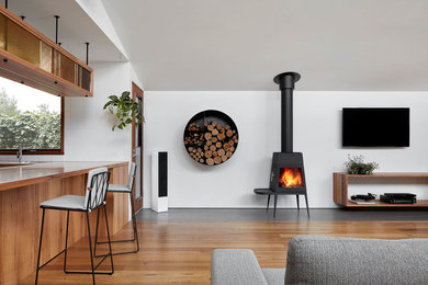 This is an example of a contemporary open plan living room in Melbourne with white walls, light hardwood flooring, a wood burning stove and a wall mounted tv.