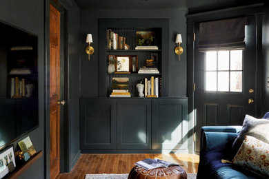 Example of a mid-sized transitional enclosed medium tone wood floor, brown floor and wainscoting living room library design in Detroit with black walls, no fireplace and a wall-mounted tv