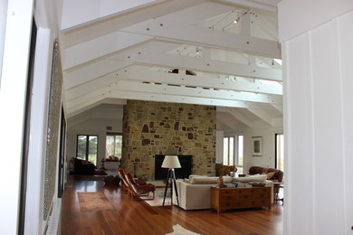 Diseño de salón abierto bohemio grande con paredes blancas, suelo de madera en tonos medios y marco de chimenea de piedra