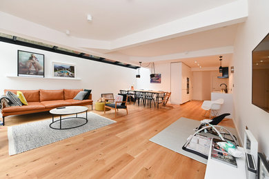 Cette image montre un grand salon design ouvert avec une salle de réception, un mur blanc, parquet clair, aucune cheminée, un manteau de cheminée en plâtre, un téléviseur fixé au mur et un sol marron.