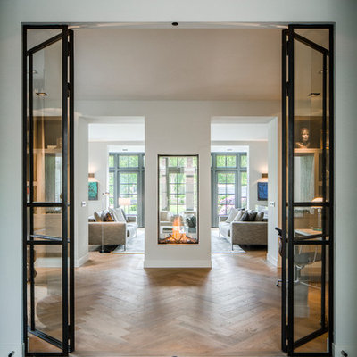 Large trendy open concept and formal medium tone wood floor and brown floor living room photo in Boston with white walls, a two-sided fireplace, a plaster fireplace and no tv