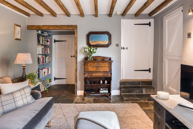 Aménagement d'un salon campagne de taille moyenne avec un mur gris, un sol en ardoise, un poêle à bois, un manteau de cheminée en brique et un sol gris.