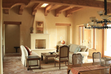 Example of a large southwest formal and open concept brick floor, brown floor, exposed beam, vaulted ceiling and wood ceiling living room design in Albuquerque with beige walls, a standard fireplace, a concrete fireplace and no tv