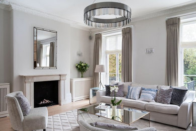 This is an example of a medium sized classic enclosed living room in London with grey walls, a standard fireplace, a stone fireplace surround, beige floors and light hardwood flooring.