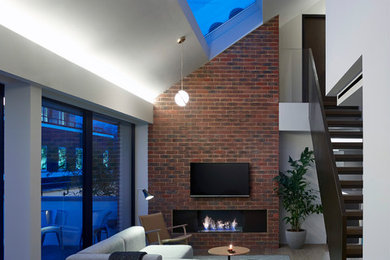 Ejemplo de salón abierto contemporáneo de tamaño medio con paredes grises, suelo de madera clara, chimenea lineal, marco de chimenea de metal y televisor colgado en la pared