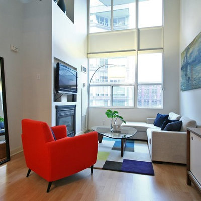 Mid-sized minimalist enclosed light wood floor and brown floor living room photo in Toronto with white walls, a wall-mounted tv, a standard fireplace and a plaster fireplace