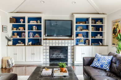 Пример оригинального дизайна: гостиная комната в современном стиле с серыми стенами, паркетным полом среднего тона, стандартным камином, фасадом камина из плитки, телевизором на стене и коричневым полом