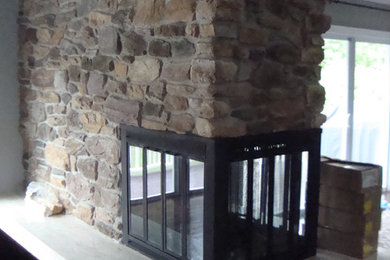 Aménagement d'un grand salon montagne ouvert avec un manteau de cheminée en pierre, un mur gris, parquet foncé et une cheminée double-face.
