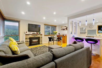 Großes, Offenes Modernes Wohnzimmer mit Hausbar, beiger Wandfarbe, braunem Holzboden, Kamin, Kaminumrandung aus Stein und TV-Wand in Melbourne