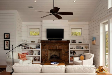 Foto di un soggiorno stile marinaro aperto con pareti bianche, pavimento in legno massello medio, camino classico, cornice del camino in mattoni e TV a parete
