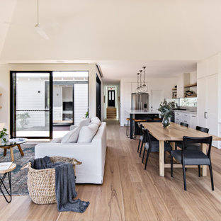Design ideas for a beach style open concept living room in Sydney with white walls, medium hardwood floors, a ribbon fireplace, a wood fireplace surround, a wall-mounted tv, brown floor and vaulted.