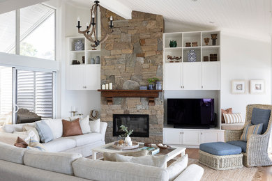 サンシャインコーストにある高級な広いトロピカルスタイルのおしゃれなLDK (白い壁、無垢フローリング、標準型暖炉、石材の暖炉まわり、据え置き型テレビ) の写真