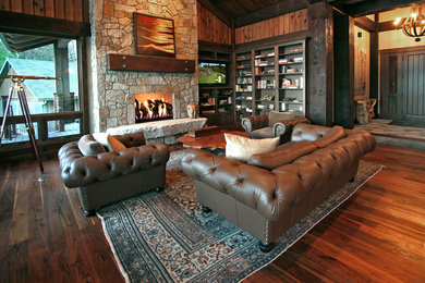 Imagen de salón abierto rural grande con paredes marrones, suelo de madera oscura, todas las chimeneas, marco de chimenea de piedra y televisor colgado en la pared
