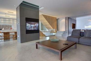 Imagen de salón abierto contemporáneo grande con paredes grises, suelo de cemento y pared multimedia