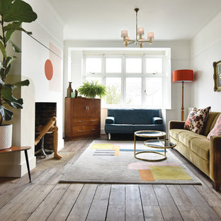Design ideas for a medium sized eclectic open plan living room in London with white walls, a concealed tv, medium hardwood flooring, a standard fireplace and brown floors.