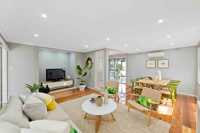 Imagen de salón abierto costero con paredes grises, suelo de madera en tonos medios y televisor independiente