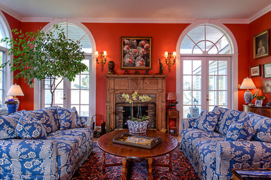 Example of a classic enclosed medium tone wood floor living room design in DC Metro with red walls, a standard fireplace and a wood fireplace surround