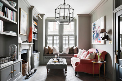 This is an example of a medium sized traditional enclosed living room in London with a reading nook, grey walls, a standard fireplace, a metal fireplace surround, medium hardwood flooring, a freestanding tv and brown floors.