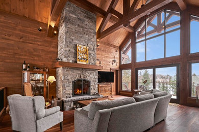 Example of a mid-sized mountain style open concept dark wood floor and brown floor living room design in Montreal with brown walls, a stone fireplace, a tv stand and a standard fireplace