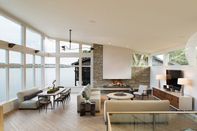 Example of a large trendy open concept light wood floor and brown floor living room design in Nashville with beige walls, a hanging fireplace, a stone fireplace and a wall-mounted tv