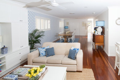 Modelo de salón abierto marinero de tamaño medio con paredes blancas, suelo de madera en tonos medios y pared multimedia