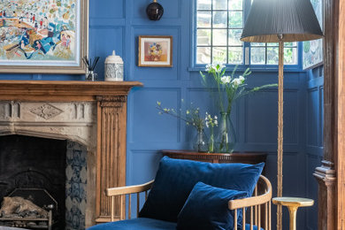 Example of a large eclectic enclosed light wood floor, beige floor, exposed beam and wood wall living room library design in London with blue walls, a standard fireplace, a stone fireplace and a concealed tv