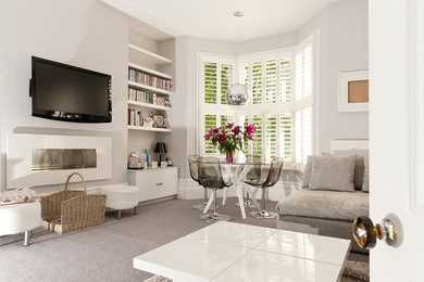 Immagine di un soggiorno minimal di medie dimensioni con pareti beige, moquette, camino sospeso, TV a parete e pavimento beige