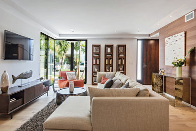 Diseño de salón abierto actual grande con paredes blancas, suelo de madera clara y televisor colgado en la pared