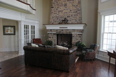 Modelo de salón para visitas abierto clásico grande con paredes beige, suelo de madera oscura, marco de chimenea de piedra y pared multimedia