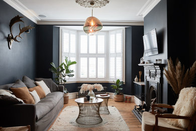 Imagen de salón clásico renovado con paredes negras, suelo de madera en tonos medios, todas las chimeneas, televisor colgado en la pared y suelo marrón