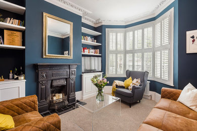 This is an example of a classic formal enclosed living room in London with blue walls, carpet, a standard fireplace, a freestanding tv and beige floors.