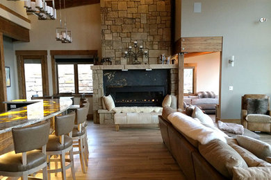 Modelo de salón abierto rústico grande con paredes beige, suelo de madera clara, chimenea lineal, marco de chimenea de piedra y suelo marrón