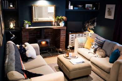 コーンウォールにある低価格の小さなトラディショナルスタイルのおしゃれなリビング (青い壁、カーペット敷き、薪ストーブ、レンガの暖炉まわり、据え置き型テレビ、ベージュの床) の写真