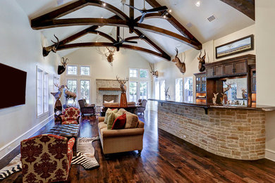 Living room - large traditional open concept medium tone wood floor, brown floor and exposed beam living room idea in Houston with a bar, beige walls, a standard fireplace, a brick fireplace and a wall-mounted tv