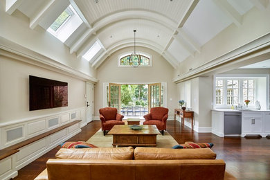 Modelo de salón clásico con paredes beige, suelo de madera en tonos medios, televisor colgado en la pared y suelo marrón