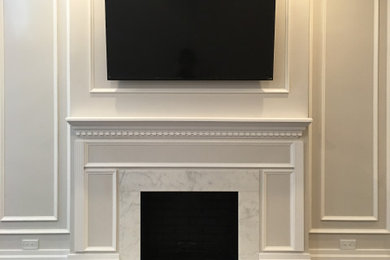 ニューヨークにある高級な中くらいなトラディショナルスタイルのおしゃれなリビング (グレーの壁、濃色無垢フローリング、標準型暖炉、石材の暖炉まわり、壁掛け型テレビ、茶色い床) の写真