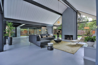 Example of a large 1950s formal and open concept concrete floor and gray floor living room design in Other with gray walls, a standard fireplace, a plaster fireplace and a wall-mounted tv