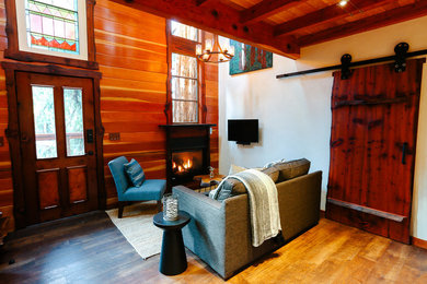 Example of a small mountain style loft-style vinyl floor living room design in San Francisco with white walls, a standard fireplace, a wood fireplace surround and a wall-mounted tv