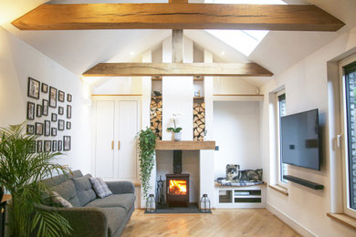 Modelo de salón abierto y abovedado escandinavo pequeño con paredes blancas, suelo de madera clara, estufa de leña, marco de chimenea de yeso y televisor colgado en la pared