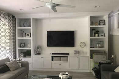 Large contemporary enclosed living room in Miami with grey walls, medium hardwood flooring, no fireplace, a wall mounted tv and grey floors.