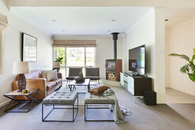 Modern inredning av ett stort separat vardagsrum, med beige väggar, heltäckningsmatta, en öppen vedspis, en spiselkrans i metall, en fristående TV och beiget golv