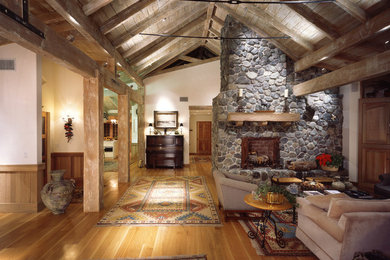 Rustik inredning av ett vardagsrum, med mellanmörkt trägolv, en standard öppen spis och en spiselkrans i sten
