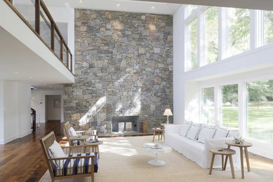 Aménagement d'un grand salon contemporain ouvert avec une cheminée standard, un manteau de cheminée en pierre, aucun téléviseur, un mur blanc, un sol en bois brun et un mur en pierre.