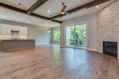 Geräumiges, Offenes Klassisches Wohnzimmer mit grauer Wandfarbe, braunem Holzboden, Kamin, Kaminumrandung aus Stein und braunem Boden in Dallas