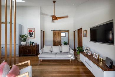 Modelo de salón abierto moderno de tamaño medio sin chimenea con paredes blancas, suelo de madera en tonos medios y televisor colgado en la pared