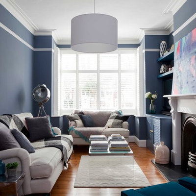 Inspiration for a mid-sized transitional enclosed medium tone wood floor and brown floor living room remodel in London with blue walls, a standard fireplace, a wood fireplace surround and no tv