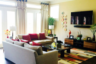На фото: большая парадная, открытая гостиная комната в классическом стиле с желтыми стенами, темным паркетным полом, телевизором на стене и коричневым полом без камина с