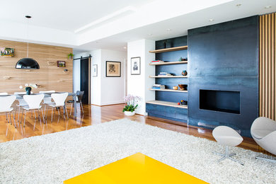 Cette image montre un grand salon minimaliste ouvert avec un mur blanc, un sol en bois brun, une cheminée standard, un manteau de cheminée en métal et un sol marron.