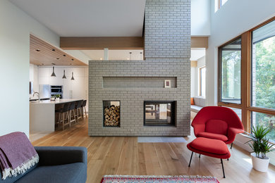 This is an example of a large contemporary open plan living room in Other with light hardwood flooring, a two-sided fireplace and a brick fireplace surround.