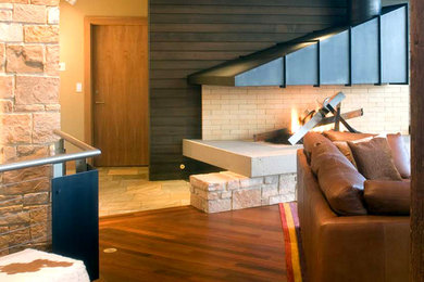 На фото: большая открытая гостиная комната в стиле модернизм с двусторонним камином, фасадом камина из металла, коричневыми стенами и темным паркетным полом